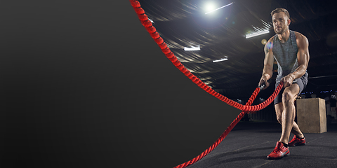 Image showing Young healthy man athlete doing exercise in the gym with ropes, flyer with copyspace