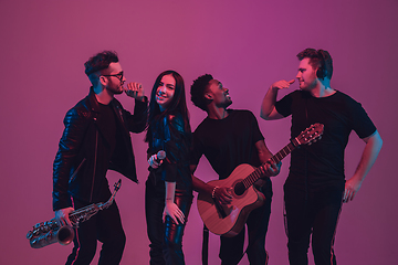 Image showing Group of young multiethnic musicians created band, dancing in neon light on pink background