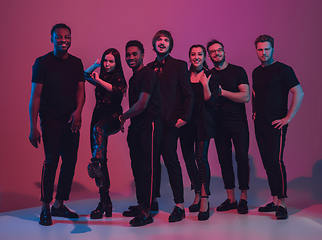 Image showing Group of young multiethnic musicians created band, dancing in neon light on pink background