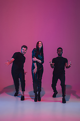 Image showing Group of young multiethnic musicians created band, dancing in neon light on pink background