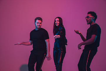 Image showing Group of young multiethnic musicians created band, dancing in neon light on pink background