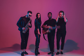 Image showing Group of young multiethnic musicians created band, dancing in neon light on pink background