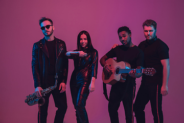 Image showing Group of young multiethnic musicians created band, dancing in neon light on pink background