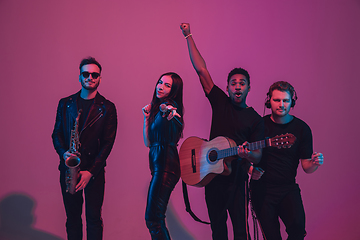 Image showing Group of young multiethnic musicians created band, dancing in neon light on pink background