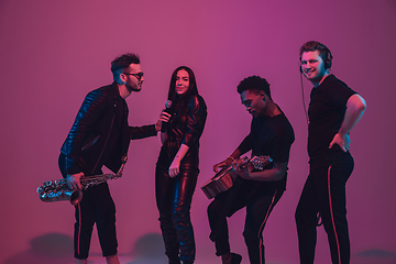 Image showing Group of young multiethnic musicians created band, dancing in neon light on pink background