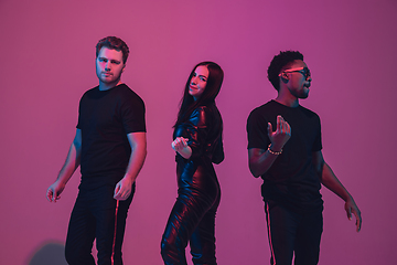 Image showing Group of young multiethnic musicians created band, dancing in neon light on pink background