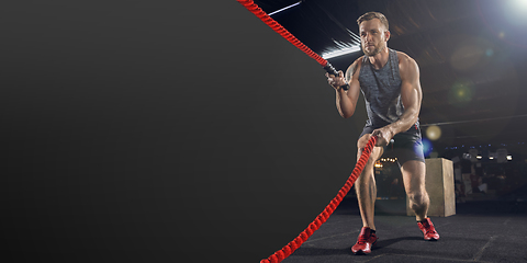 Image showing Young healthy man athlete doing exercise in the gym with ropes, flyer with copyspace