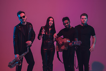 Image showing Group of young multiethnic musicians created band, dancing in neon light on pink background