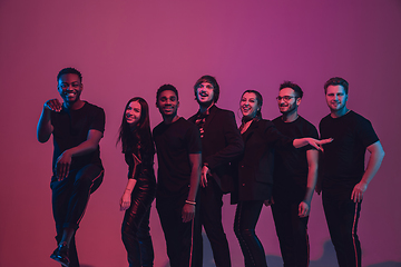 Image showing Group of young multiethnic musicians created band, dancing in neon light on pink background