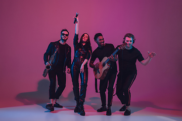 Image showing Group of young multiethnic musicians created band, dancing in neon light on pink background