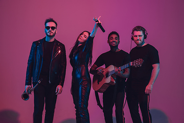 Image showing Group of young multiethnic musicians created band, dancing in neon light on pink background
