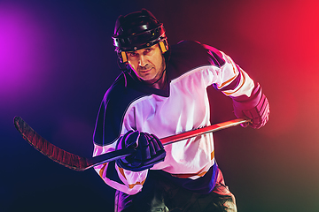 Image showing Male hockey player with the stick on ice court and dark neon colored background