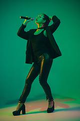 Image showing Caucasian female singer portrait isolated on green studio background in neon light