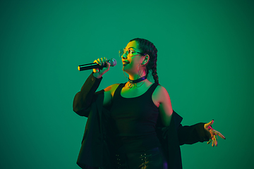 Image showing Caucasian female singer portrait isolated on green studio background in neon light