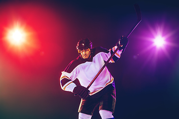 Image showing Male hockey player with the stick on ice court and dark neon colored background