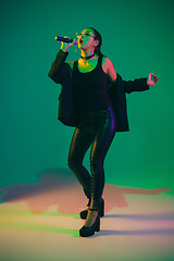 Image showing Caucasian female singer portrait isolated on green studio background in neon light