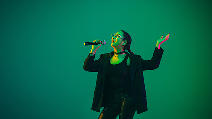 Image showing Caucasian female singer portrait isolated on green studio background in neon light