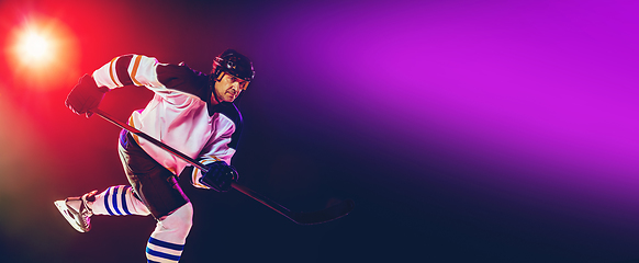 Image showing Male hockey player with the stick on ice court and dark neon colored background