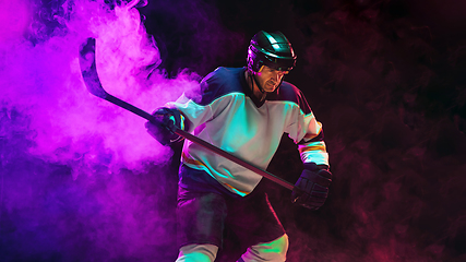 Image showing Male hockey player with the stick on ice court and dark neon colored background