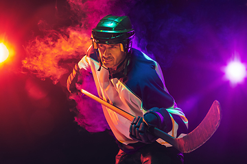 Image showing Male hockey player with the stick on ice court and dark neon colored background