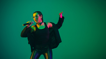 Image showing Caucasian female singer portrait isolated on green studio background in neon light