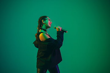 Image showing Caucasian female singer portrait isolated on green studio background in neon light