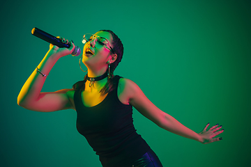 Image showing Caucasian female singer portrait isolated on green studio background in neon light