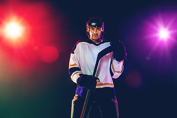 Image showing Male hockey player with the stick on ice court and dark neon colored background