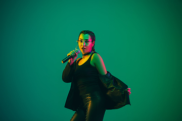 Image showing Caucasian female singer portrait isolated on green studio background in neon light