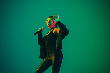 Image showing Caucasian female singer portrait isolated on green studio background in neon light