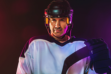 Image showing Male hockey player with the stick on ice court and dark neon colored background