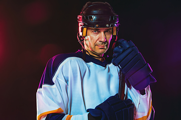 Image showing Male hockey player with the stick on ice court and dark neon colored background