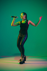 Image showing Caucasian female singer portrait isolated on green studio background in neon light