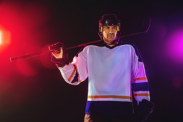 Image showing Male hockey player with the stick on ice court and dark neon colored background