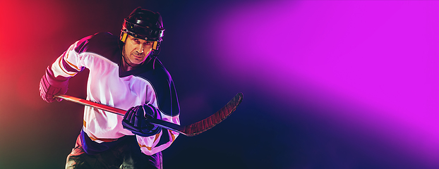 Image showing Male hockey player with the stick on ice court and dark neon colored background