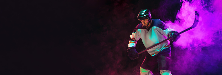 Image showing Male hockey player with the stick on ice court and dark neon colored background