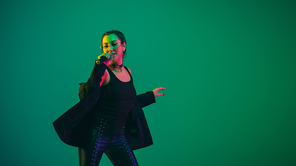 Image showing Caucasian female singer portrait isolated on green studio background in neon light