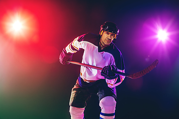 Image showing Male hockey player with the stick on ice court and dark neon colored background