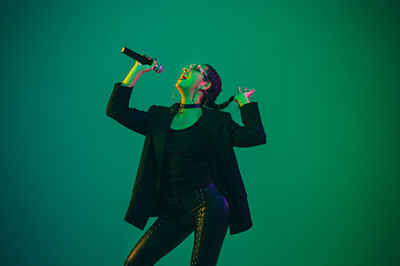 Image showing Caucasian female singer portrait isolated on green studio background in neon light