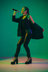 Image showing Caucasian female singer portrait isolated on green studio background in neon light