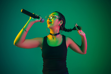 Image showing Caucasian female singer portrait isolated on green studio background in neon light