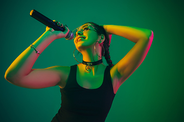 Image showing Caucasian female singer portrait isolated on green studio background in neon light