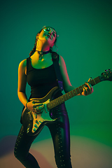 Image showing Caucasian female guitarist portrait isolated on green studio background in neon light