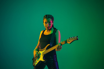 Image showing Caucasian female guitarist portrait isolated on green studio background in neon light