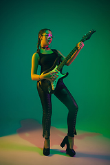 Image showing Caucasian female guitarist portrait isolated on green studio background in neon light