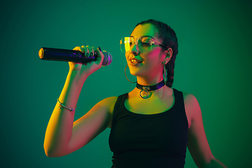 Image showing Caucasian female singer portrait isolated on green studio background in neon light