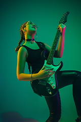 Image showing Caucasian female guitarist portrait isolated on green studio background in neon light