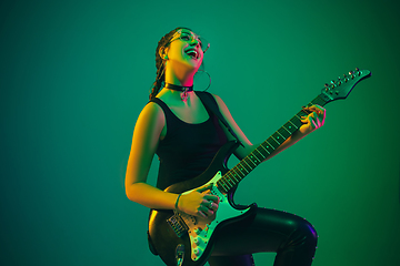 Image showing Caucasian female guitarist portrait isolated on green studio background in neon light