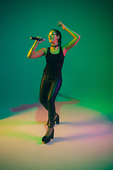 Image showing Caucasian female singer portrait isolated on green studio background in neon light