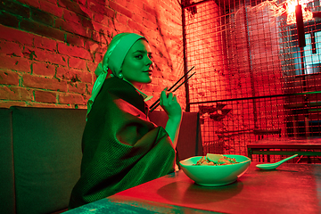 Image showing Beautiful girl with a pearl earring taking lunch in modern cafe, restaurant in neon light